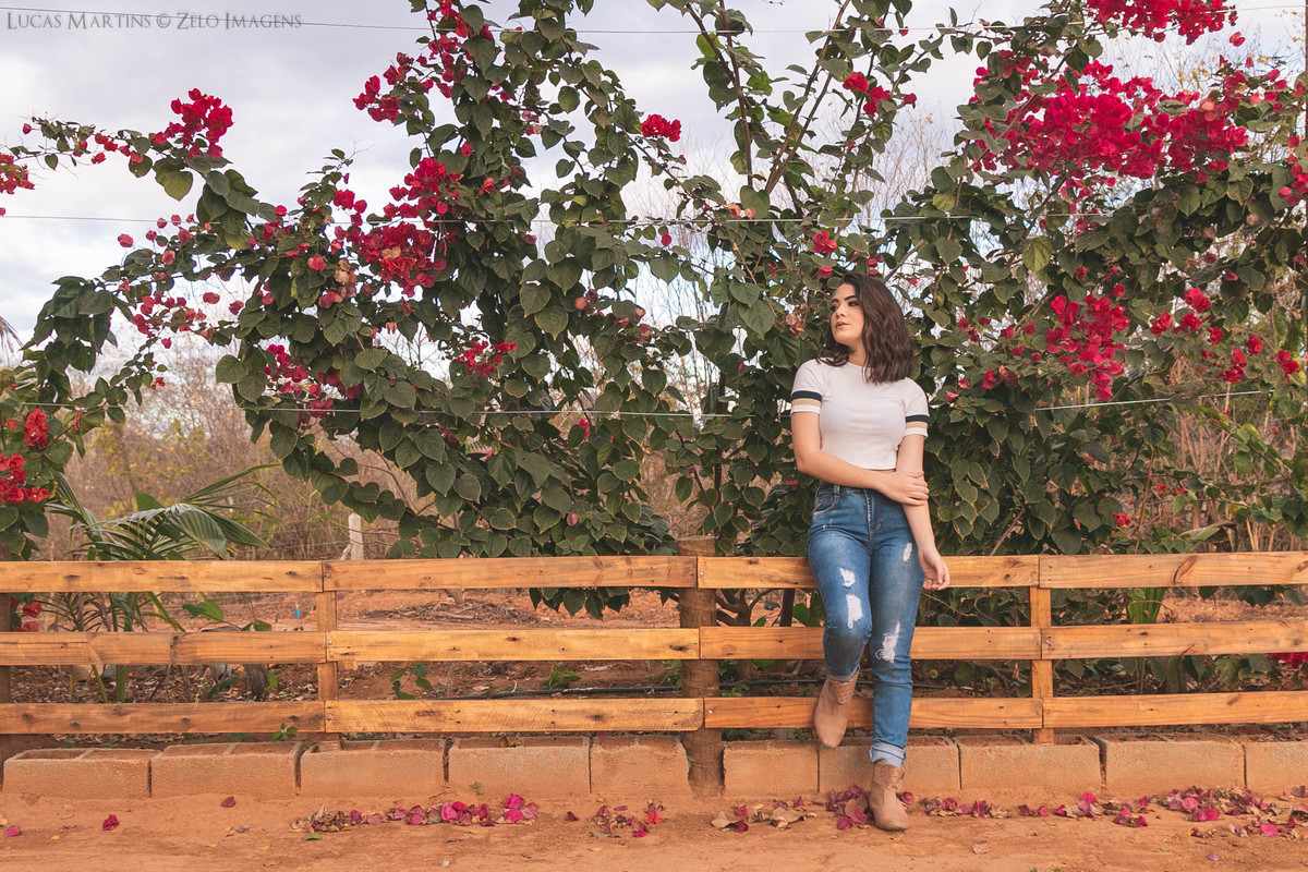 Debutante posa encostada em uma cerca com rosas ao fundo