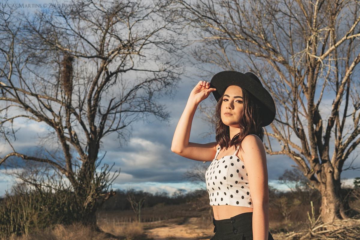 Debutante posa de chapeu perto a galhos retorcidos