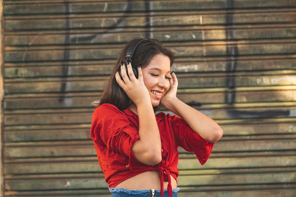 Debutante posa de saia jeans e blusa vermelha ouvindo musica pelos fones de ouvido