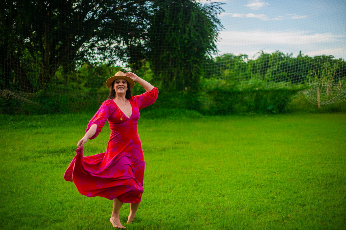 Modelo em campo verde usando chapéu de palha e vestido vermelho floral.
