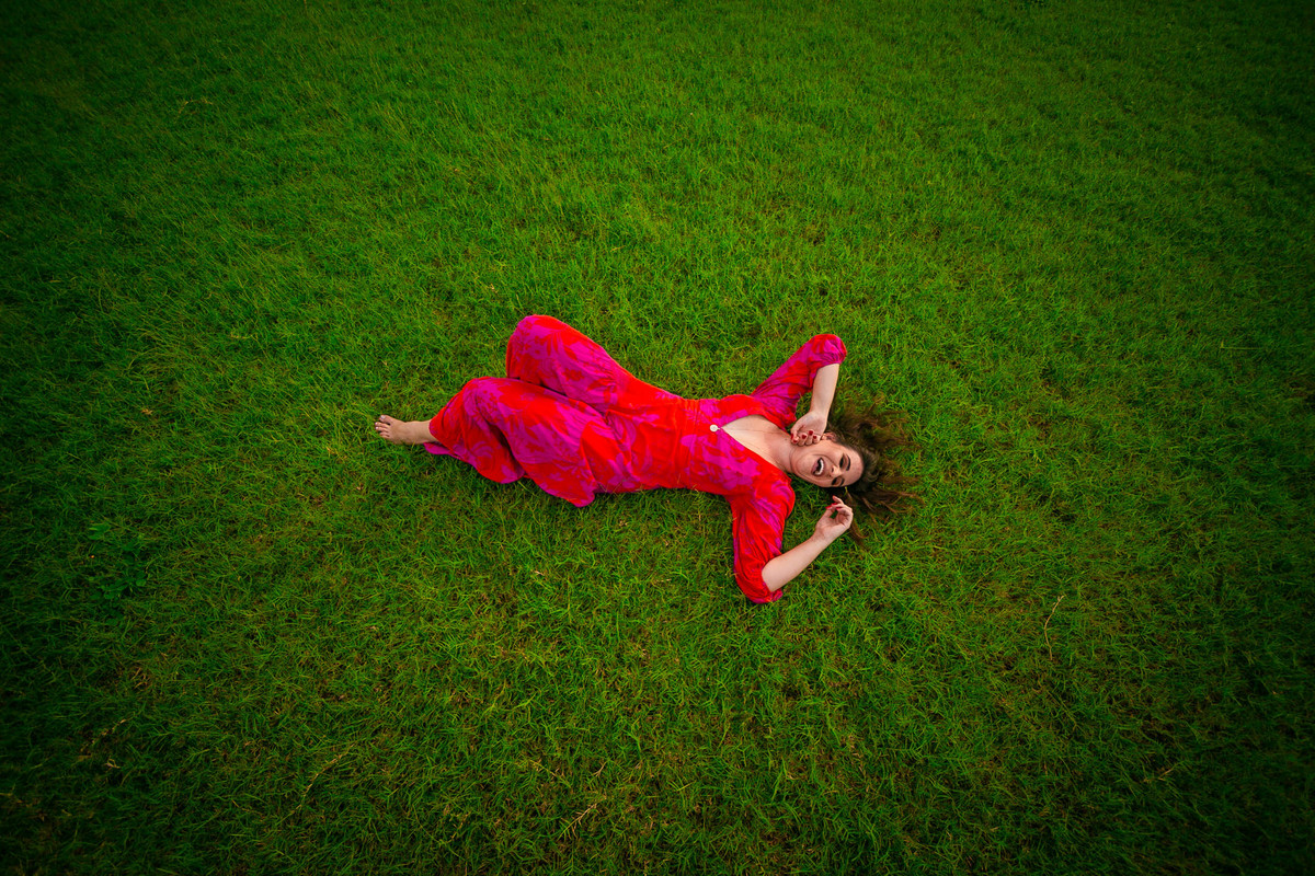 Modelo deitada em campo verde usando vestido vermelho floral.