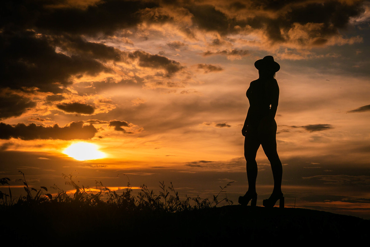 Silhueta de modelo usando chapéu de palha e salto alto ao por do sol.