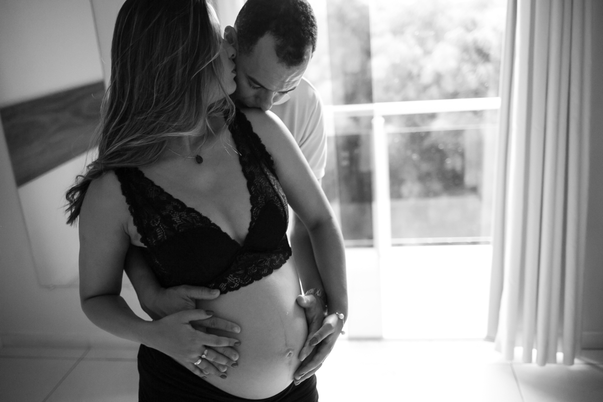 Foto em preto e branco de casal se abraçando, ambos com a mão na barriga da gestante. 