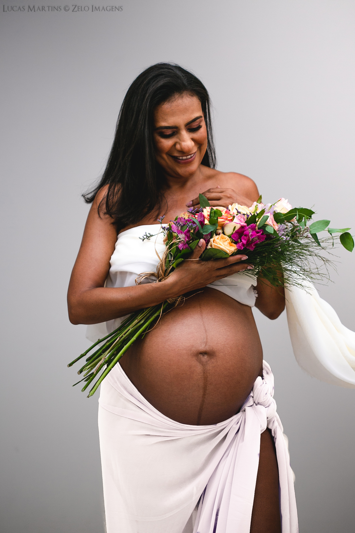 Foto em estúdio de gestante segurando junto ao  busto um buque de flores