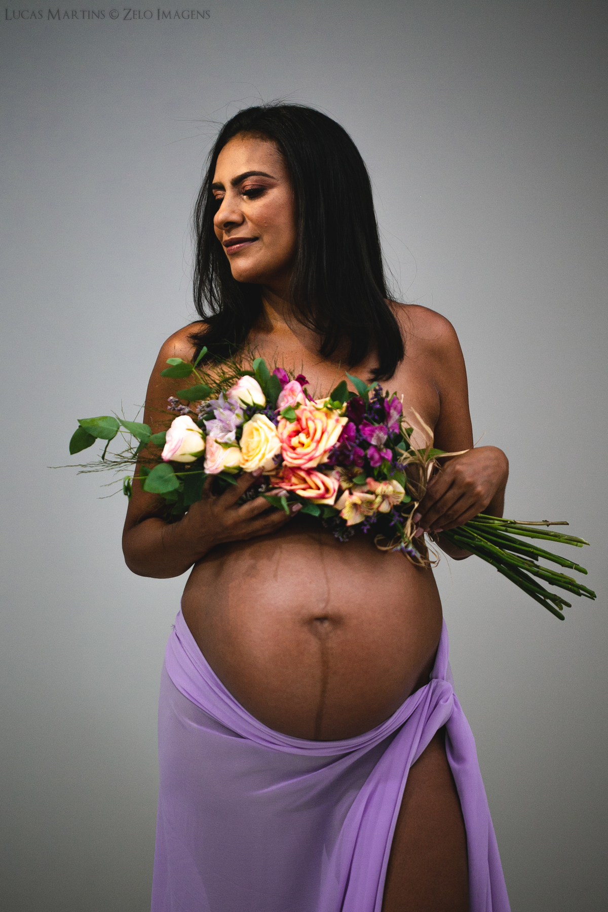 Foto em estúdio de gestante segurando junto ao  busto um buque de flores