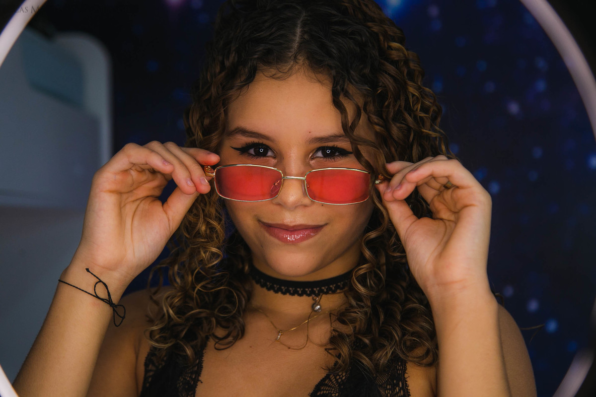 ensaio adolescente debutante maquiando em frente ao espelho e oculos com ringlight aracuai minas gerais