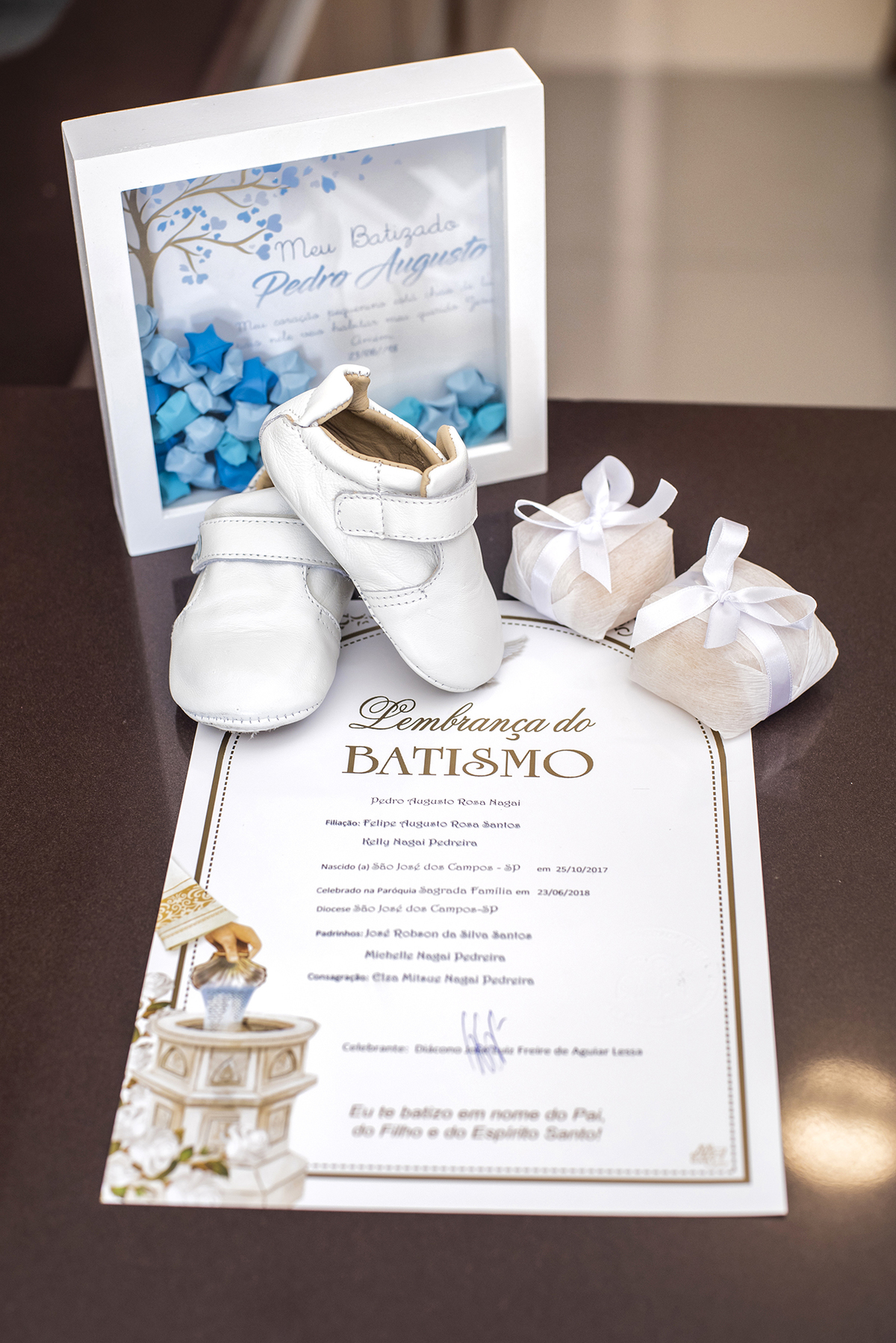 Lembrança do batismo mostra certificado , sapatinhos , vela e docinhos da festa