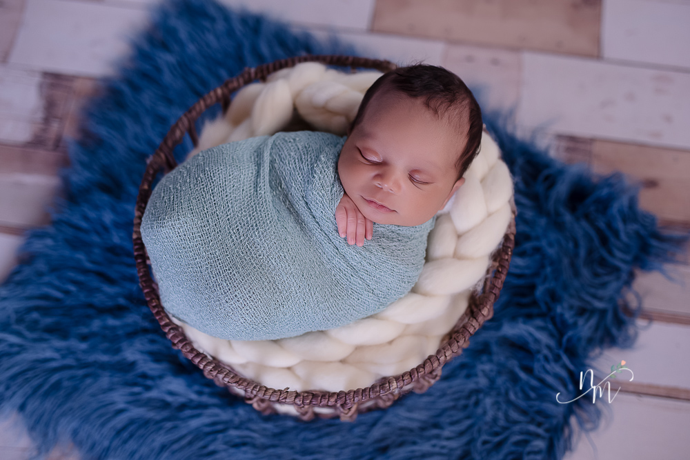 foto de bebe recem nascido enrolado num paninho azul dentro do cesto
