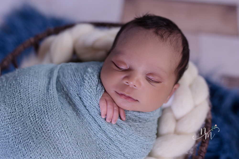 foto de bebe recem nascido enrolado num paninho azul dentro do cesto