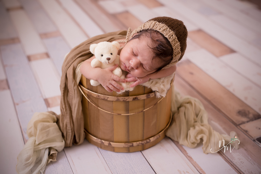 Bebê recém nascido dentro do caixote com ursinho de pelúcia na mão