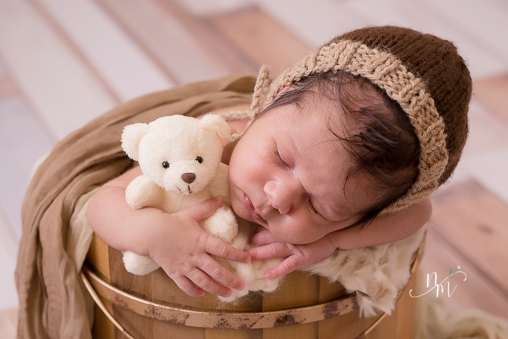 Bebê recém nascido dentro do caixote com ursinho de pelúcia na mão