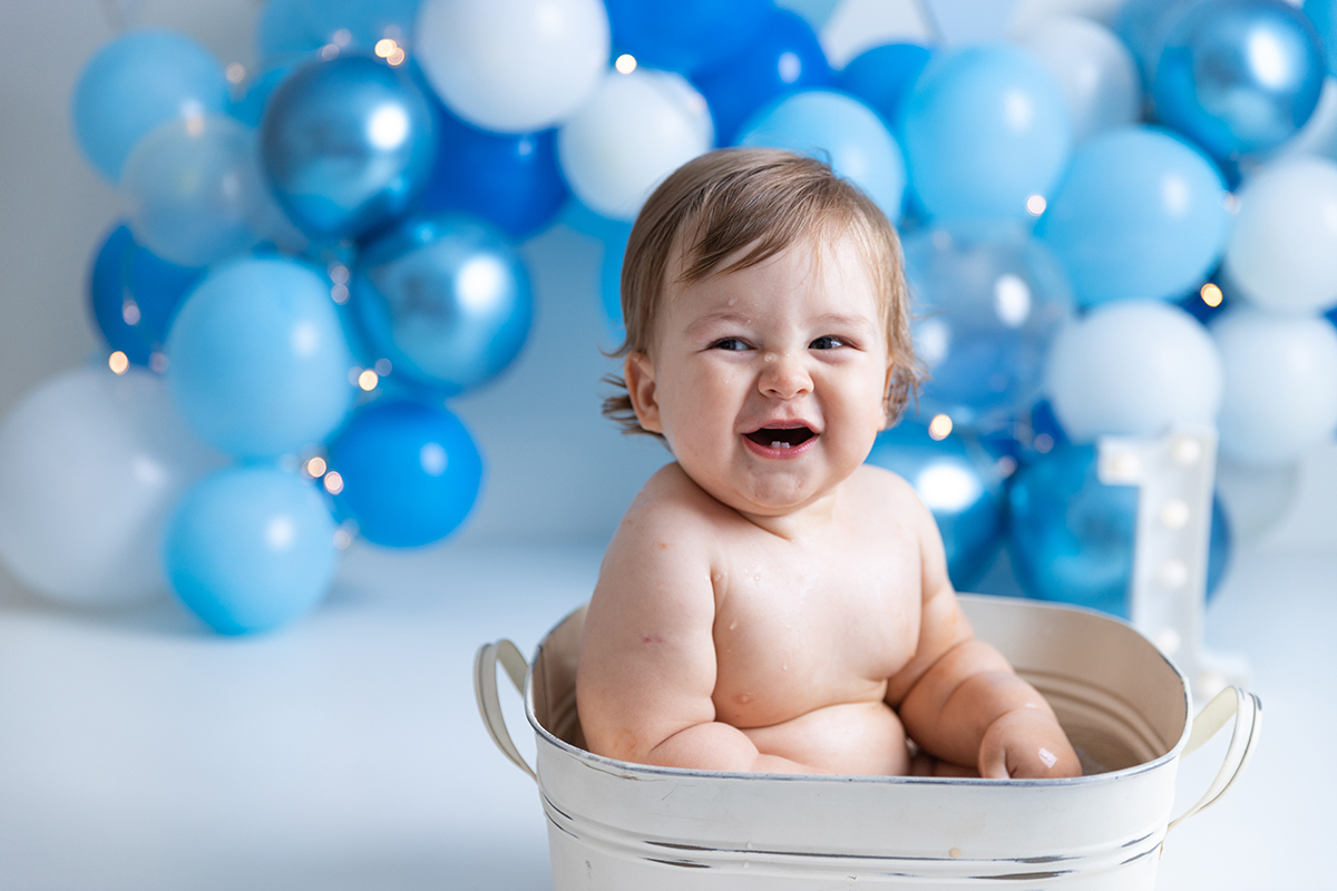 Bebê tomando banho dentro da tina no cenário de balões azul