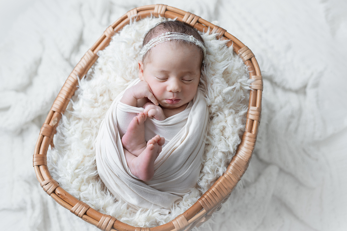 bebê recém nascida dormindo enroladinha no tecido branco dentro de um cestinho