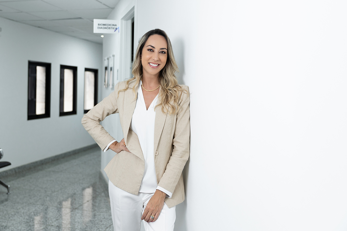 Biomédica de blazer bege encostada numa parede branca