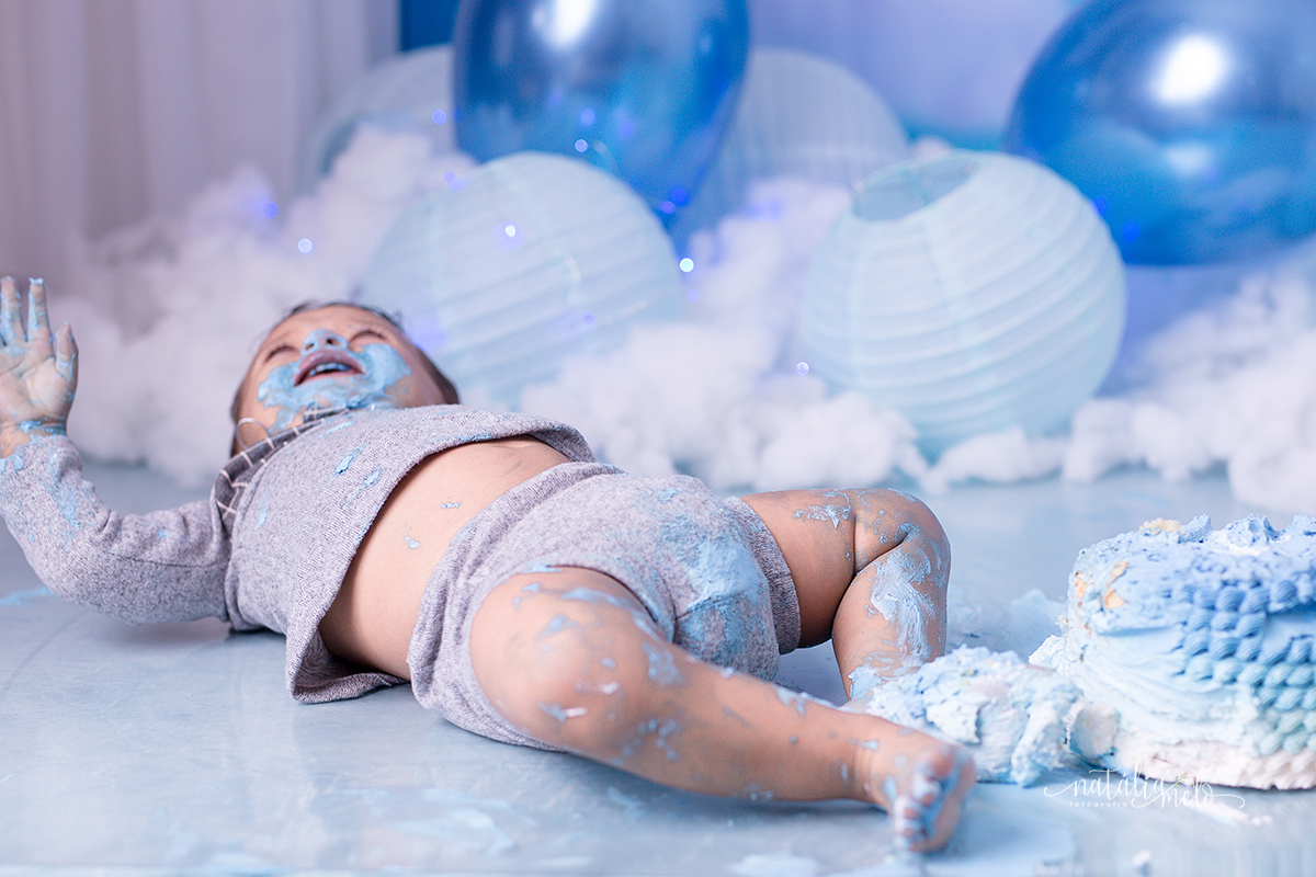 bebê deitado no chão todo sujo de bolo no Ensaio smash the cake no tema Balões feito no Estúdio Natália Melo Fotografia em Belo Horizonte - MG