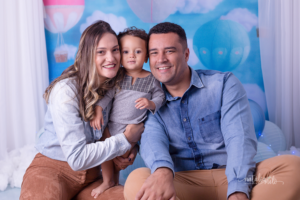 Pai e mãe abraçados com filho num cenário de balões no Estúdio Natália Melo Fotografia em Belo Horizonte -