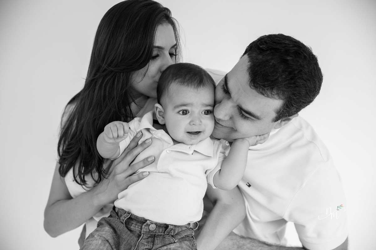 Ensaio de família feito por Natália Melo Fotografia, em Belo Horizonte -MG, onde pai e mãe carregam filho no colo e dão um beijo de cada lado.