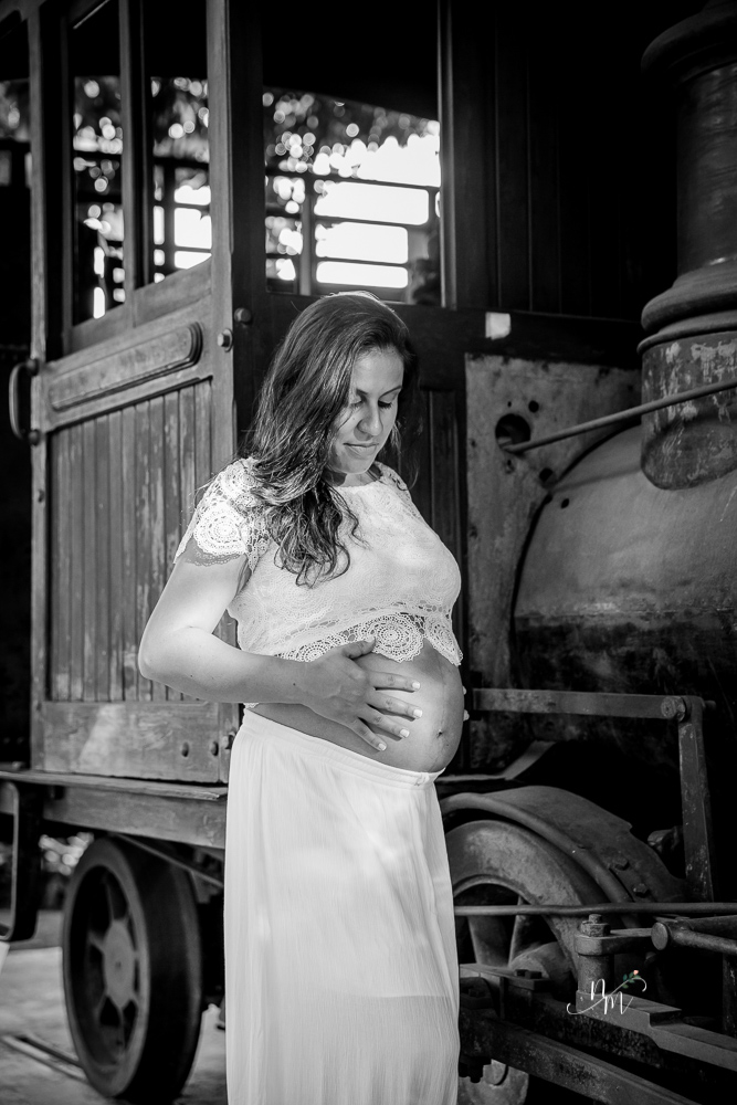 ensaio de gestante feito por Natália Melo Fotografia em Belo Horizonte -MG, no Museu Histórico Abílio Barreto, onde a Flaviana em frente a uma locomotiva olhando para a barriga