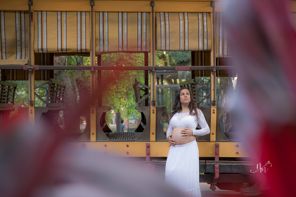 ensaio de gestante feito por Natália Melo Fotografia em Belo Horizonte -MG, no Museu Histórico Abílio Barreto, onde a Flaviana entre os bancos de um bonde ohando para a barriga