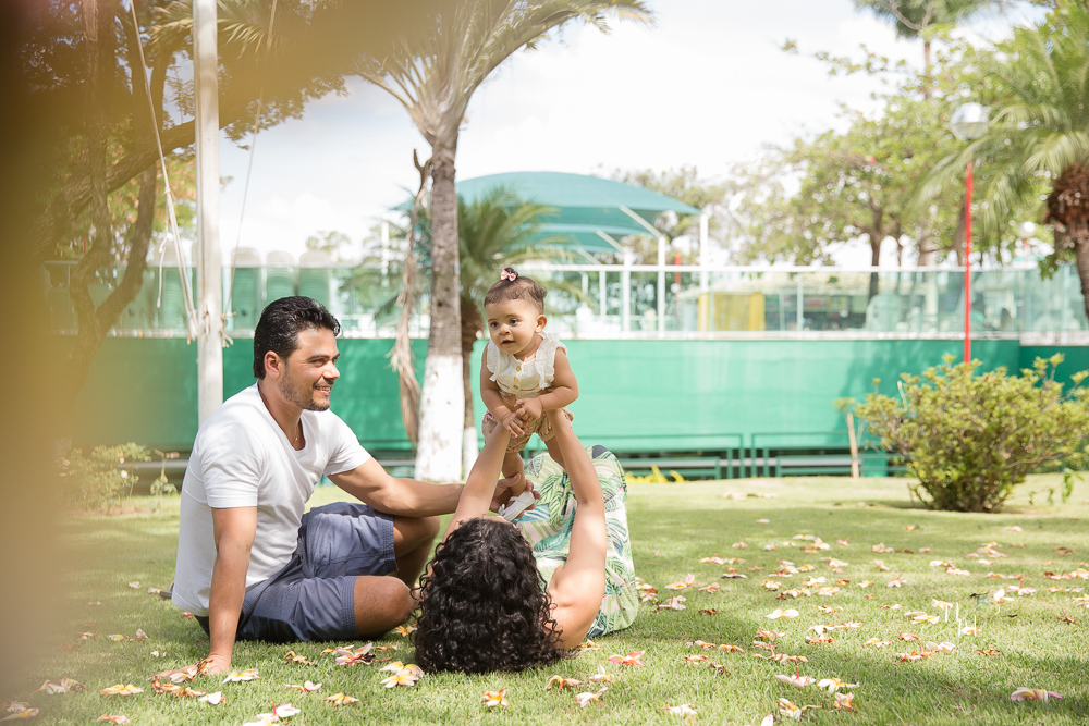 Ensaio de Família feito por Natália Melo Fotografia no Clube Jaraguá em Belo Horizonte - MG, onde pai e mãe carregam Lara e brincam com ela no colo deitados no gramad