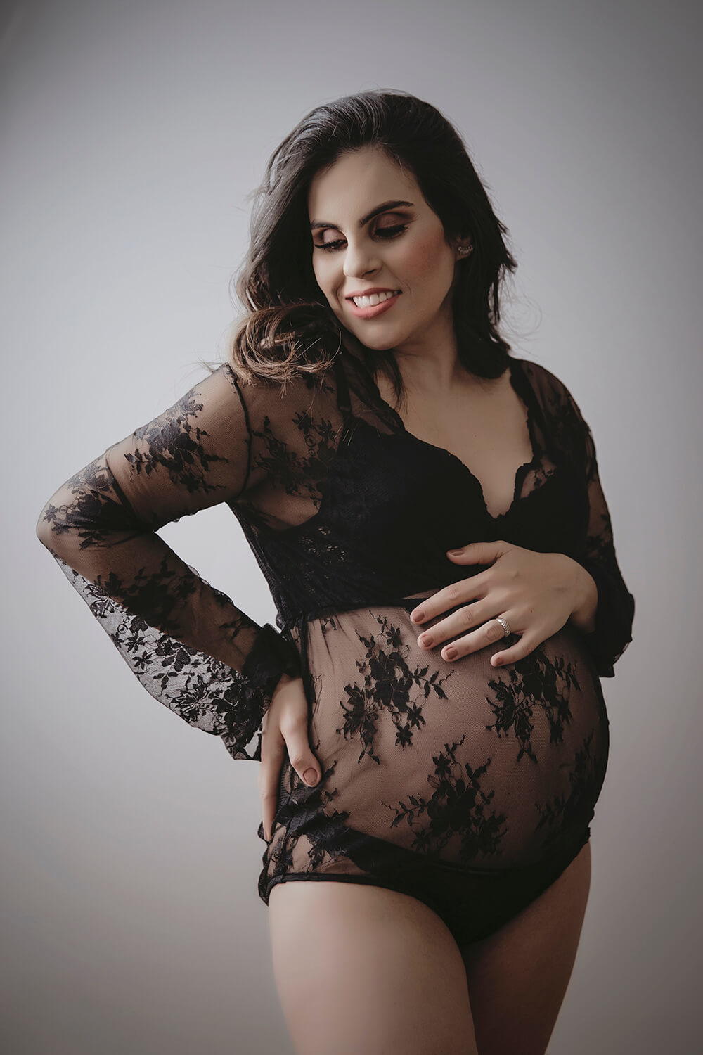 Gestante de lingerie preta com a mão na barriga no estúdio Natália Melo - Fotografia