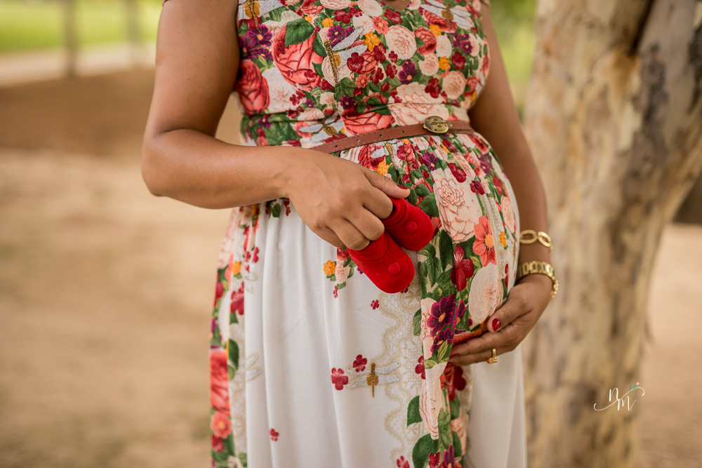 Gestante segurando um sapatinho do bebê em uma área verde em Belo Horizonte  - MG fotografada por Natália Melo