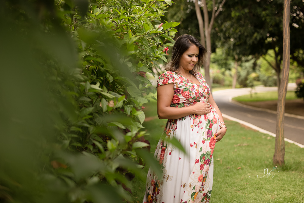 Gestante olhando para a barriga em uma área verde em Belo Horizonte  - MG fotografada por Natália Melo