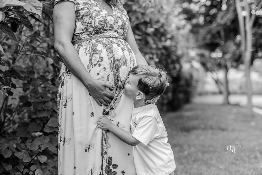 Gestante junto com seu primeiro filho beijando a barriga em uma área verde em Belo Horizonte  - MG fotografada por Natália Melo