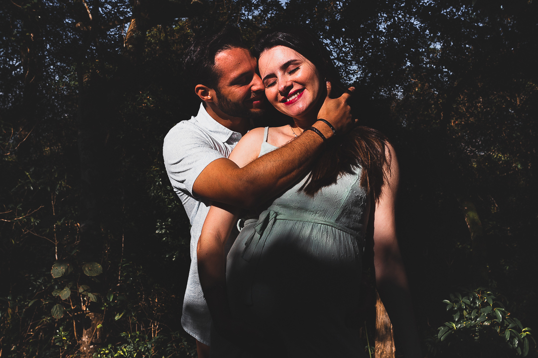 casal gestante, com mãos na barriga, na floresta