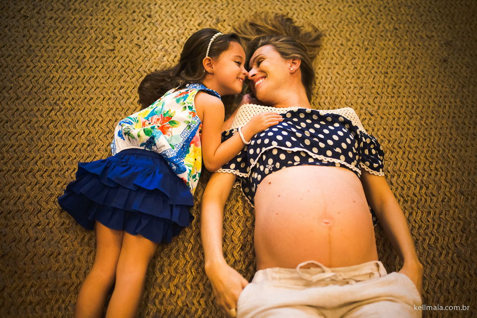 Gestante beija a filha, deitada no tapete