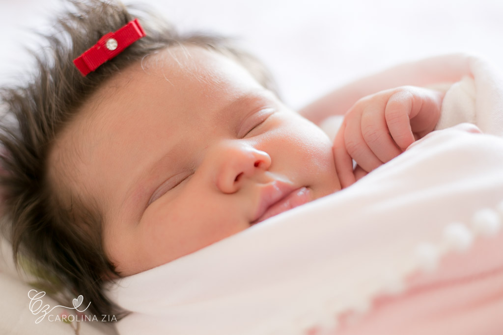 Bebê recém nascida Liz dorme tranquilamente em sua sessão de newborn aos 9 dias de vida Rosa branco e laço vermelho