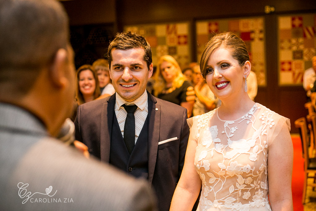Noivos sorriem ao receber a benção de seu casamento. Noiva de off-while Anna Kara, estilista de vestidos de noiva Polonesa. Maquiagem natural e batom pink para noiva.