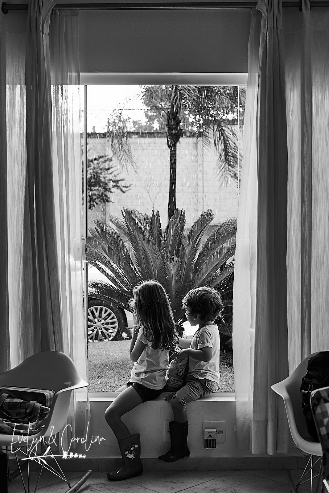 crianças de galocha observam a chuva forte que cai