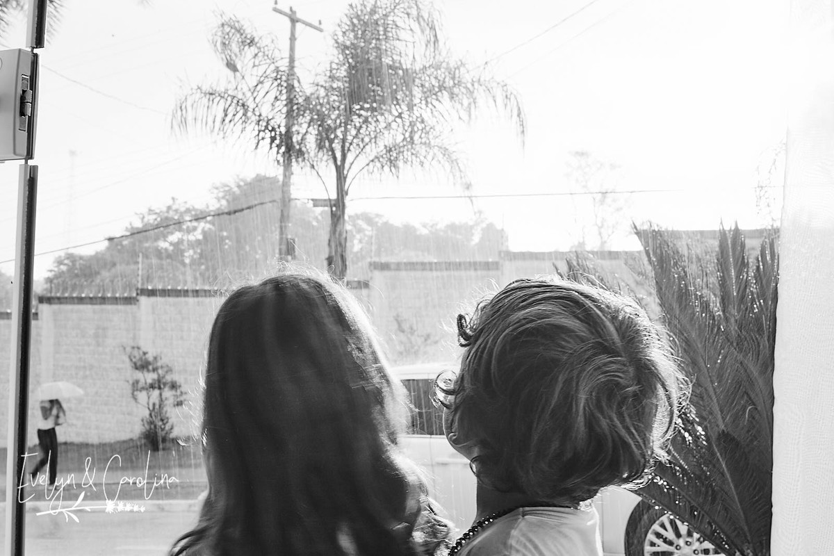 irmãos se abraçam ao ver chuva pela janela em fotografia documental de família