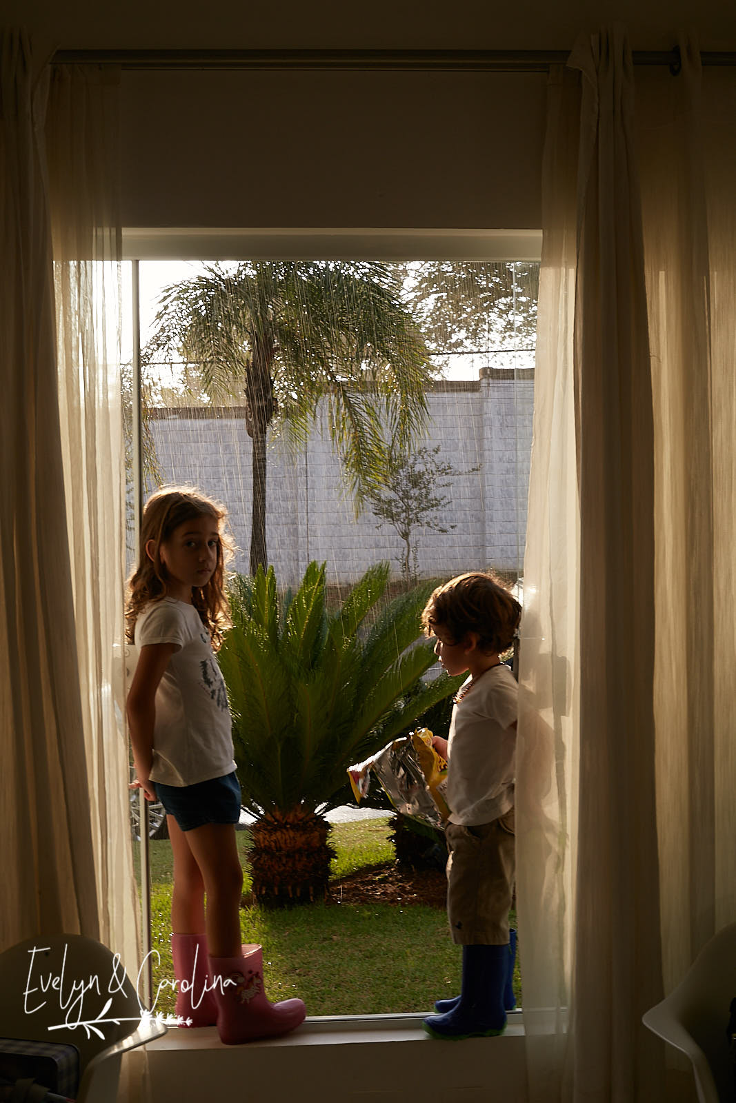 irmãos observam a chuva enquanto estão sentados na janela