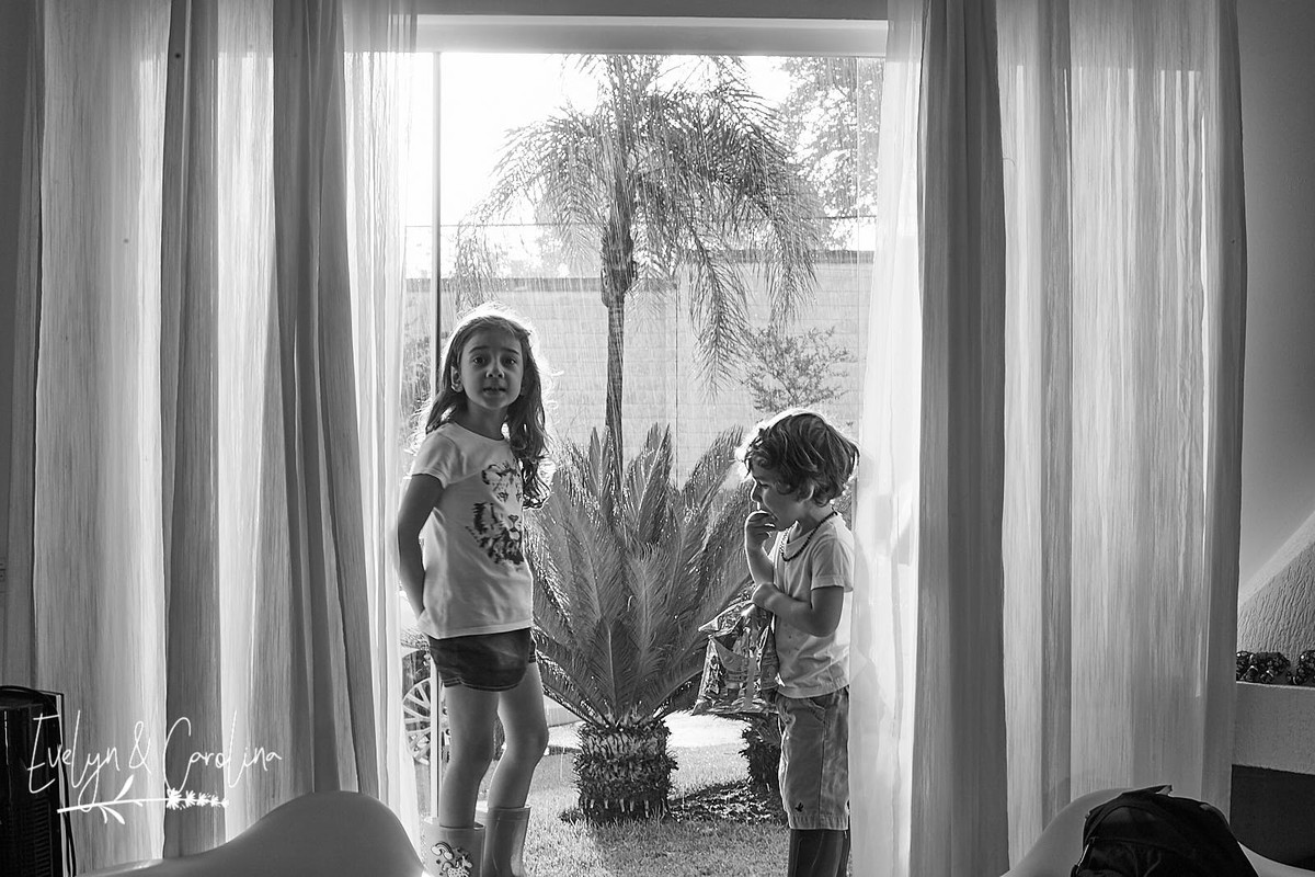 irmãos observam a chuva enquanto estão sentados na janela