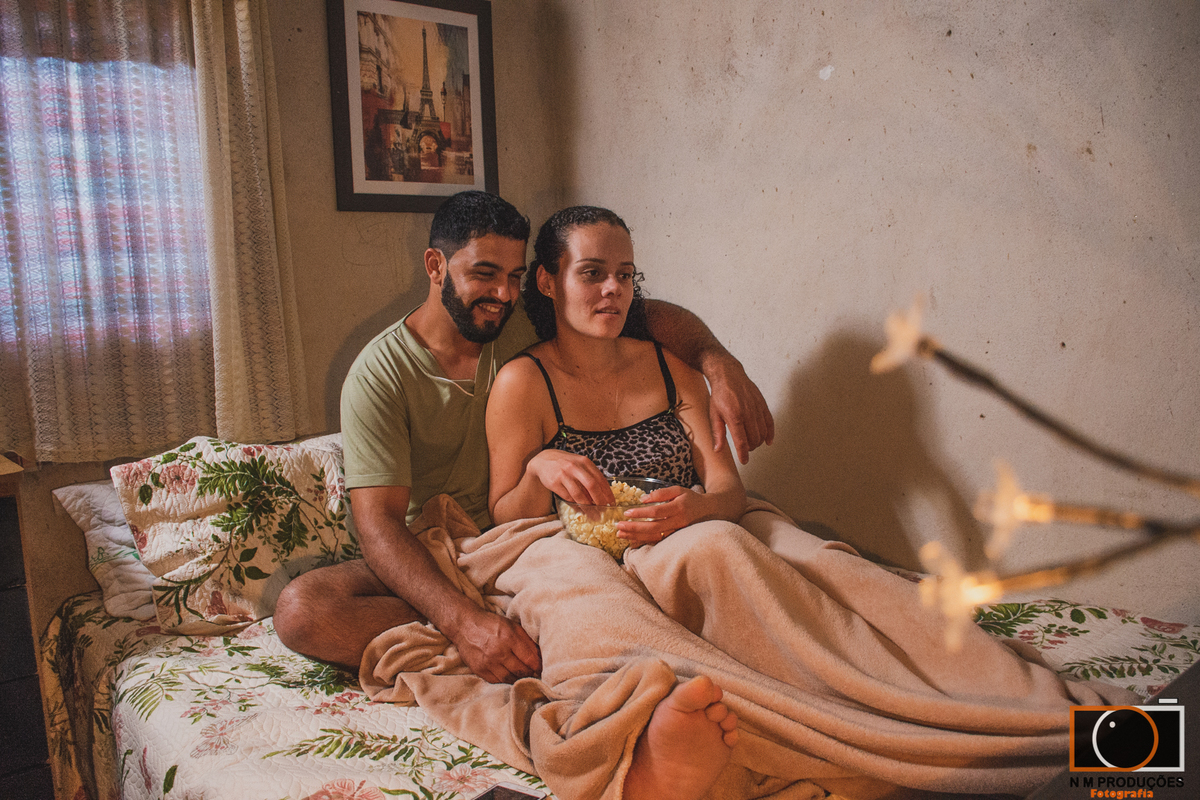 Casal Marina e Welington na cama vendo filme com pipoca
