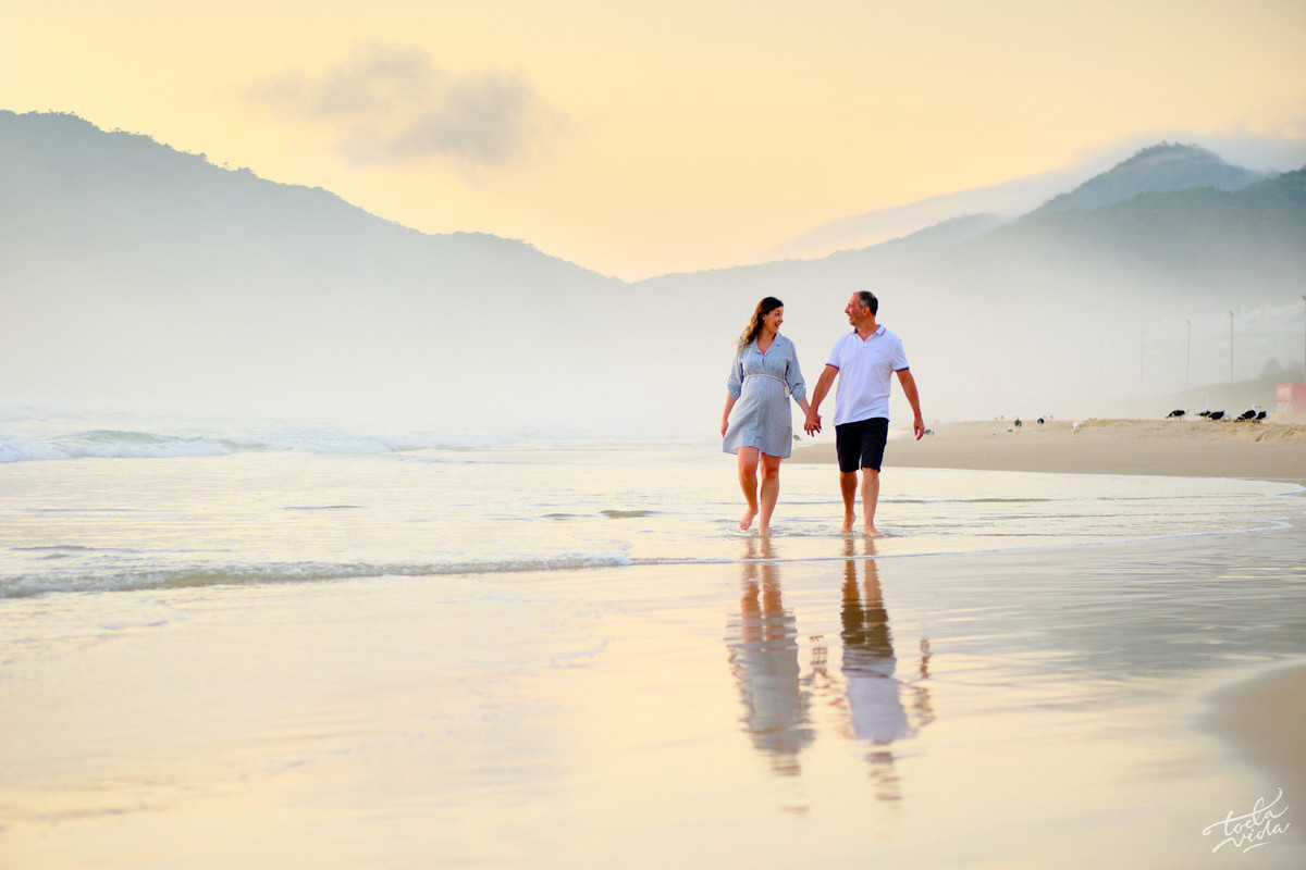 casal gestante caminhando na praia ao amanhecer