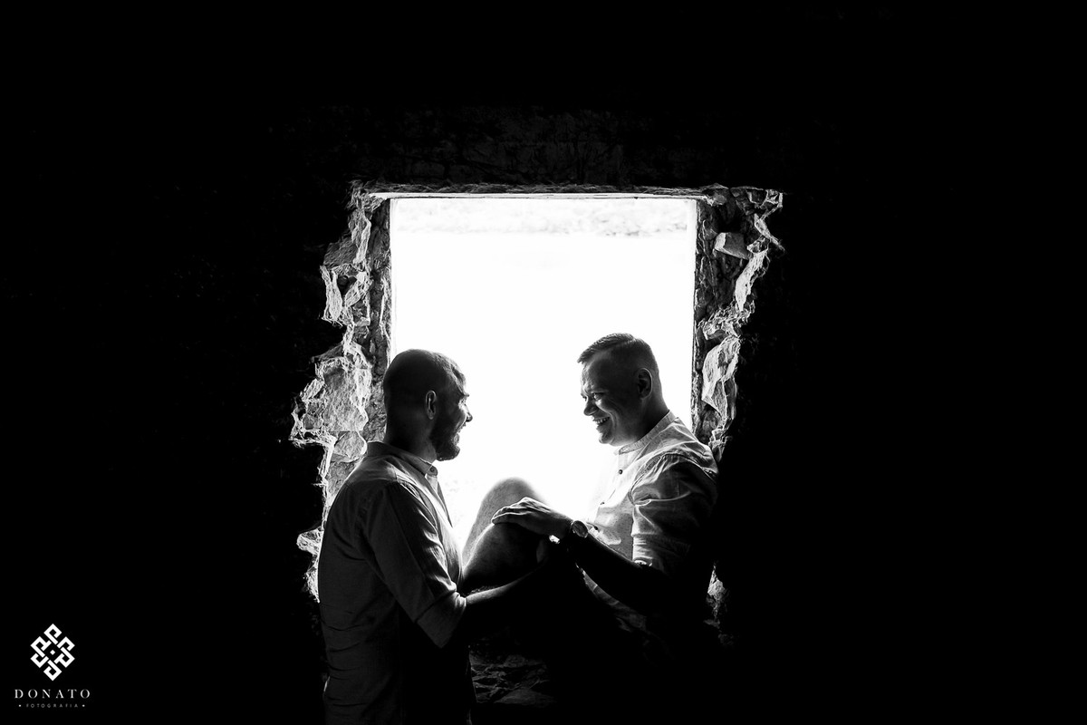 o casal senta na janela, onde entra um luz muito bonita.