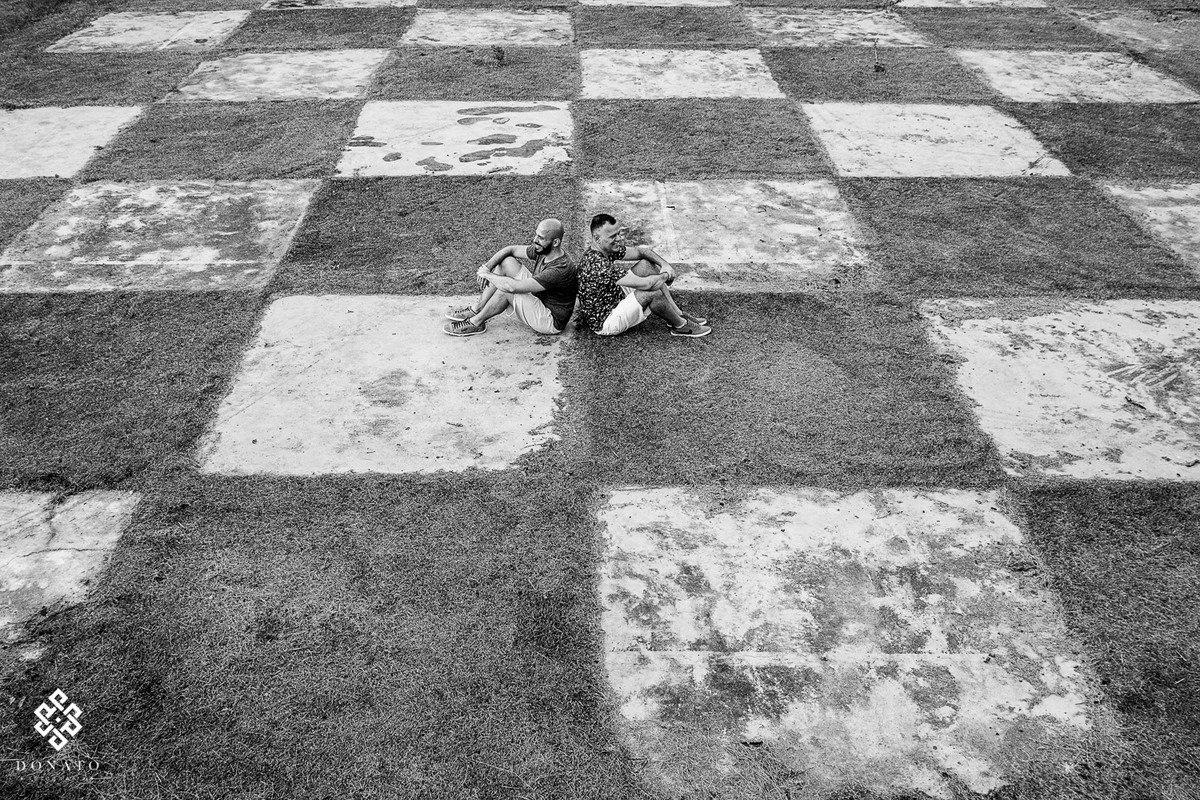 o casal esta sentado no chão com enormes figuras quadradas, que forma um tabuleiro.