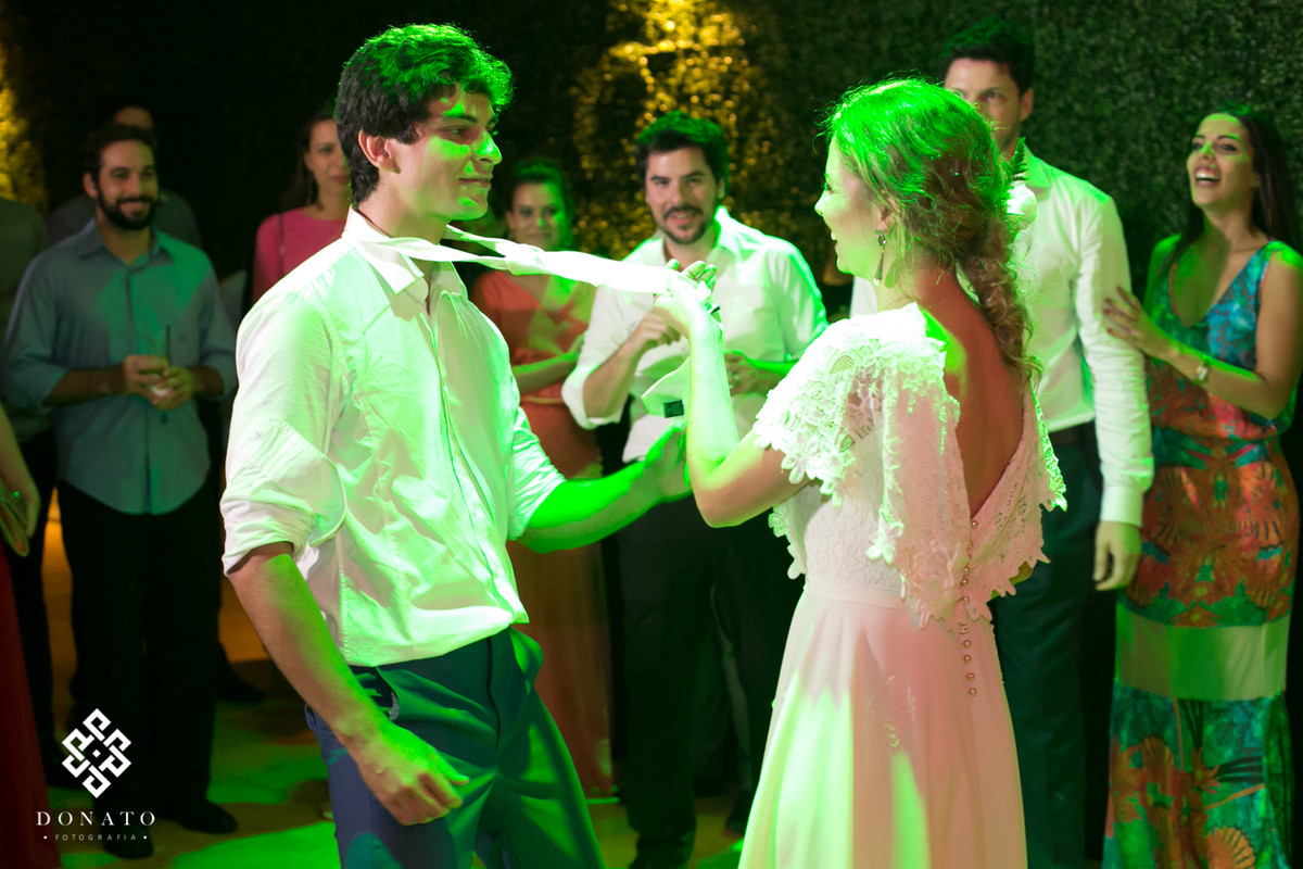 Noiva dança com o noivo, agarrando ele pela gravata.