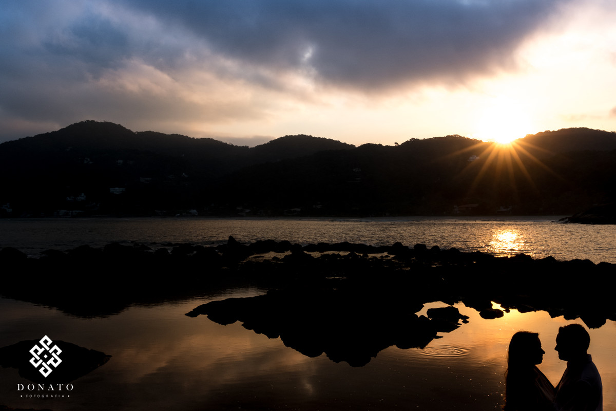 foto do lindo por do sol da praia do guaruja, com o mar ao fundo e com o casal e silheta todo escuro a frente.