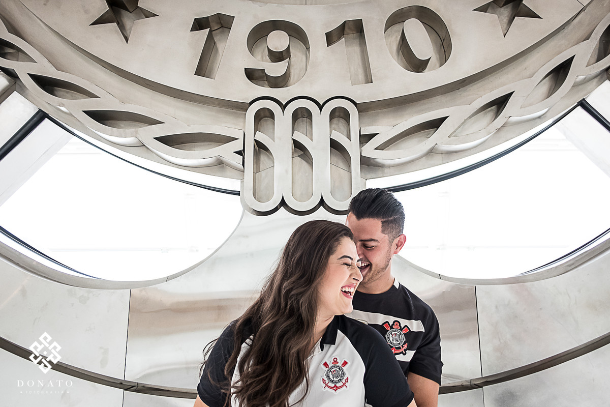 Retrato sorrindo dos noivos em frente ao simbolo do corinthians.