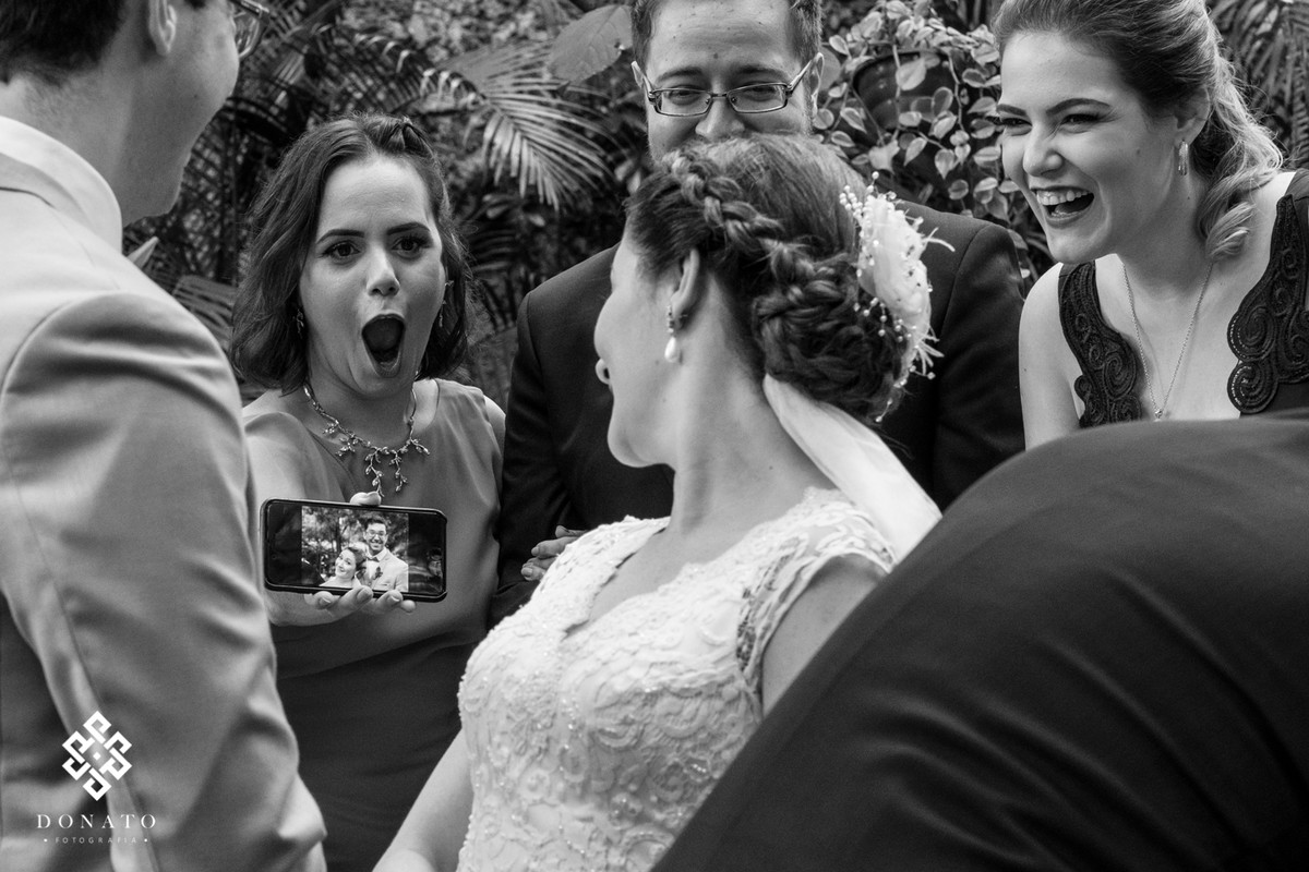 Madrina mostra foto que acabou de fazer no celular e faz uma cara de espanto.