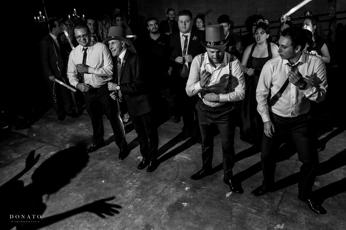 Noivo e amigos dançam, enquanto uma sombra dança junto com eles.
