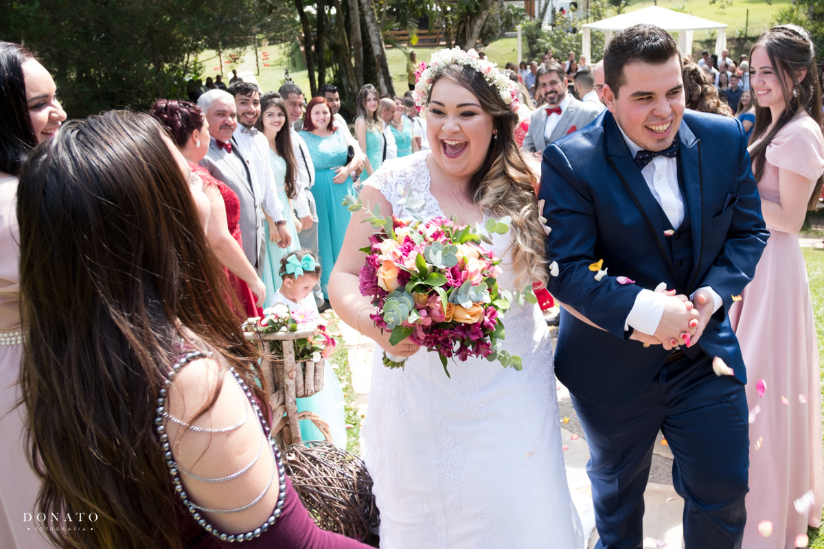 Noivo e noiva saem e recebem uma linda chuva de petalas, em meio a natureza e arvores.