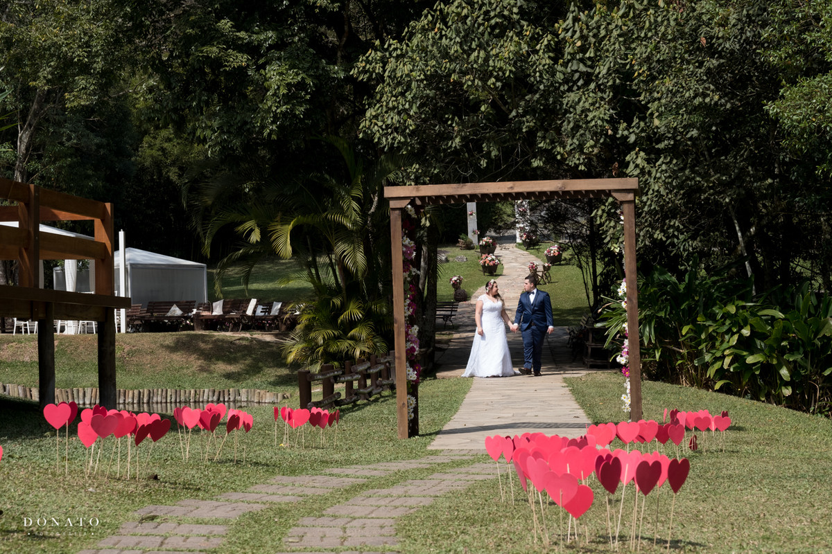 Noivos entram entre corações colocados no chao do espaço natureza.