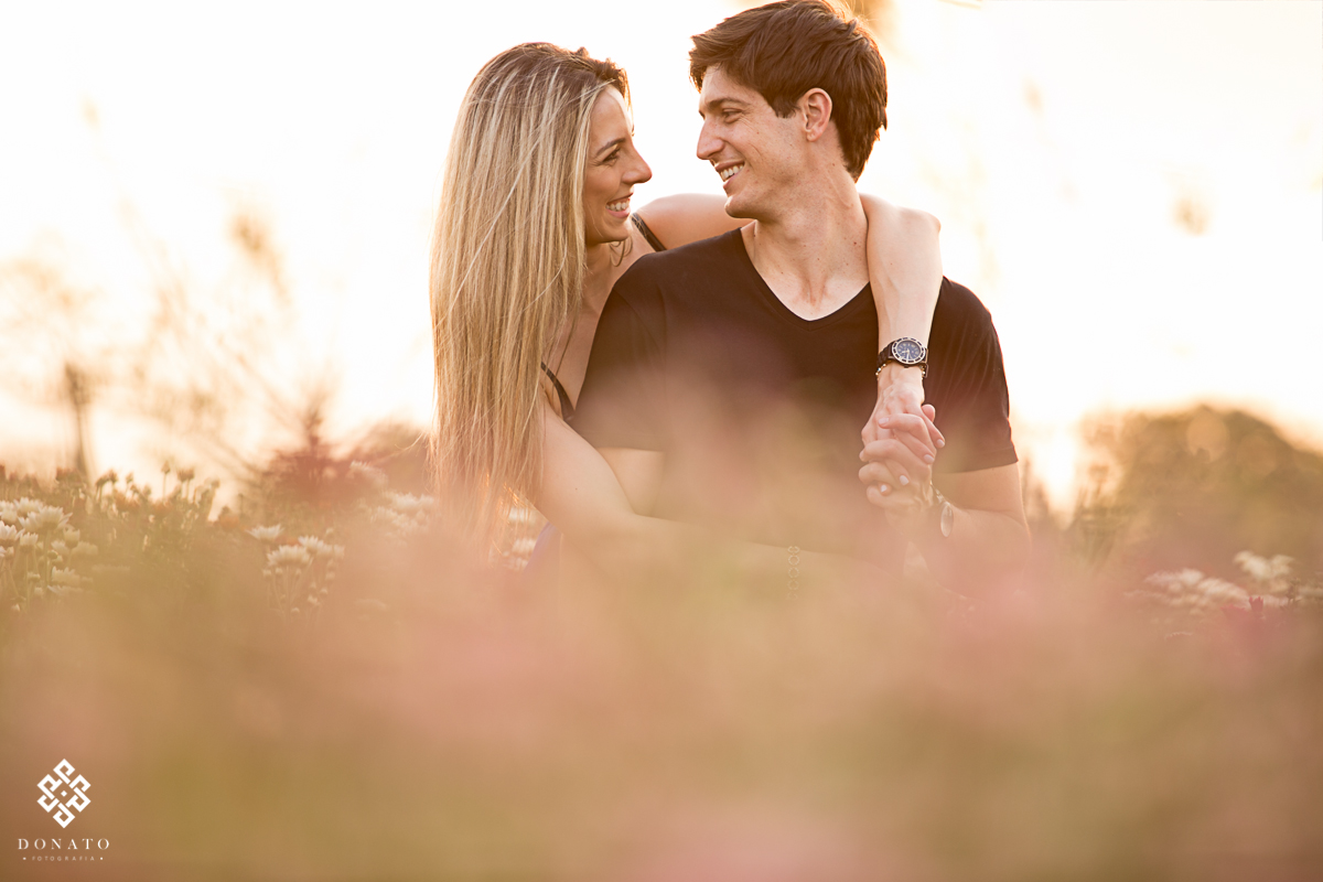 noivos namoram ao por do sol, o abraço da noiva por trás deixa a imagem linda.