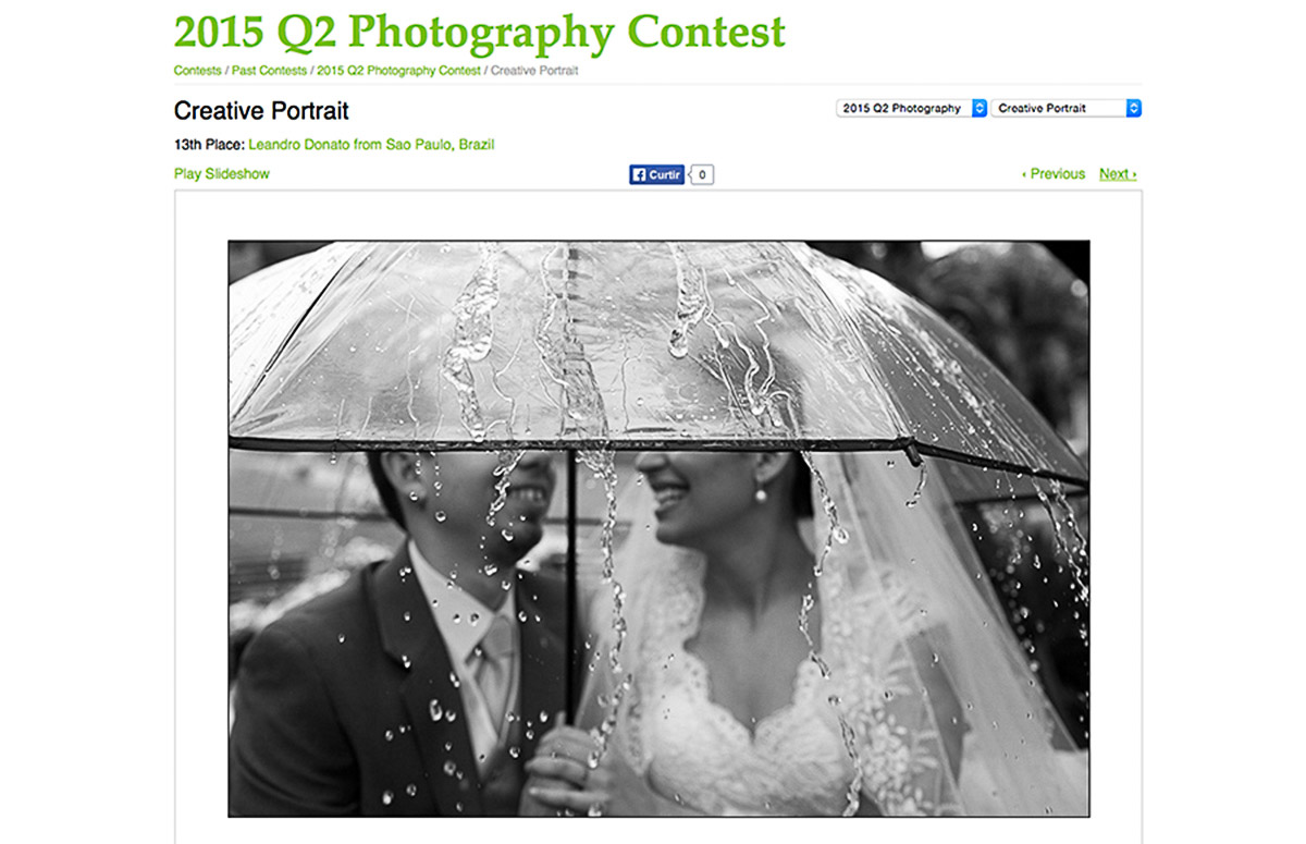 Noivos com guarda chuva, e a agua caindo forte e molhando tudo, os noivos ao fundo se diverte com a situação, a foto foi premiada no Fearless.