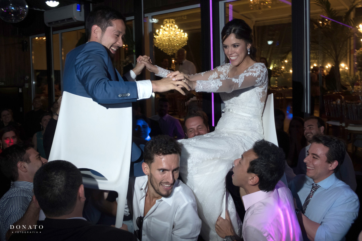 Convidados levantam os noivos em cadeiras no meio da festa.